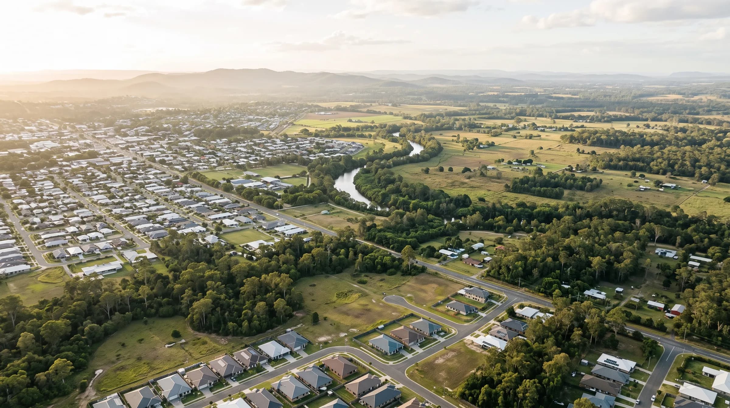 Aerial view of a semi-rural Queensland town edge with suburban streets giving way to paddocks and a river