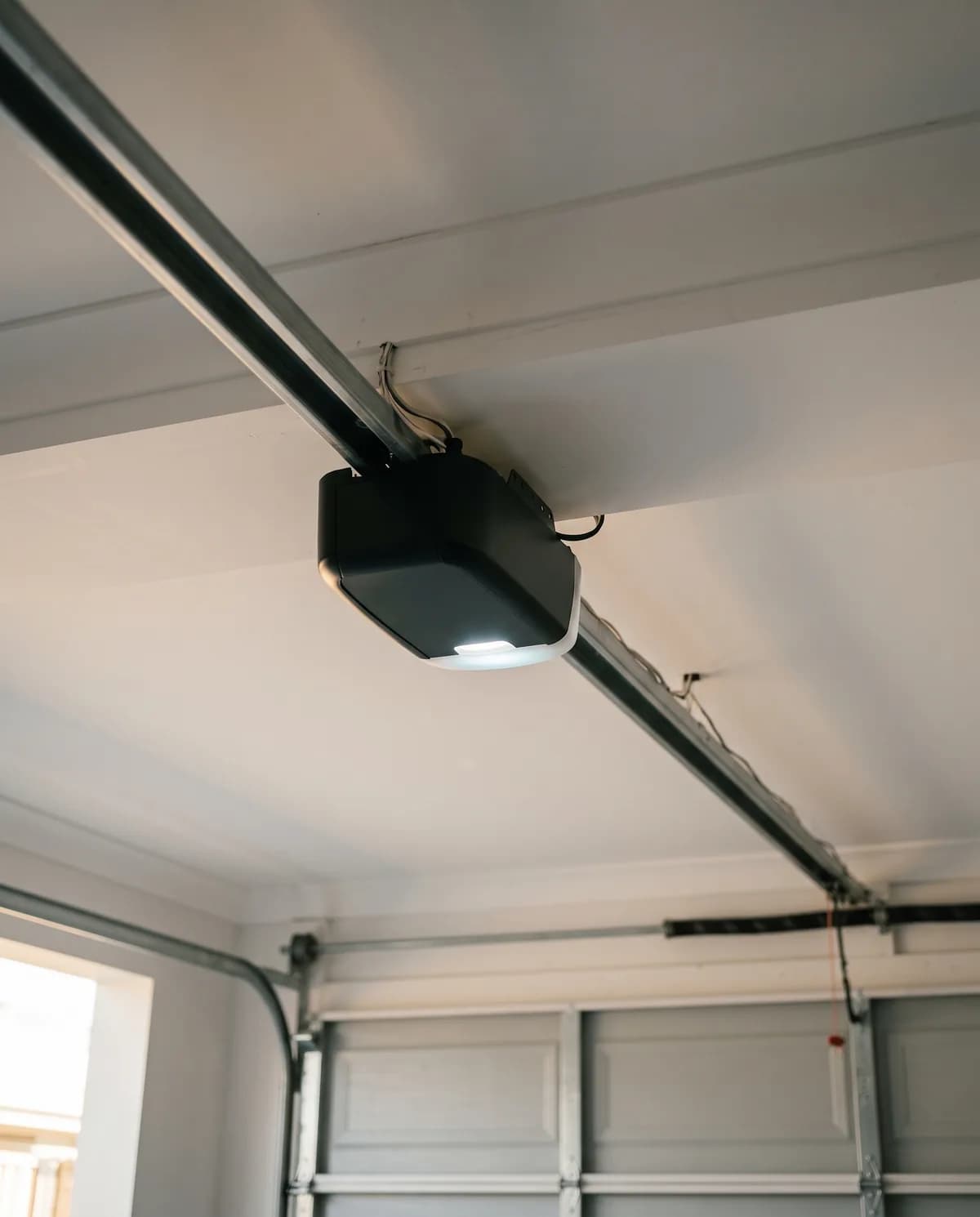 A modern garage door opener drive unit on its rail with the courtesy light on